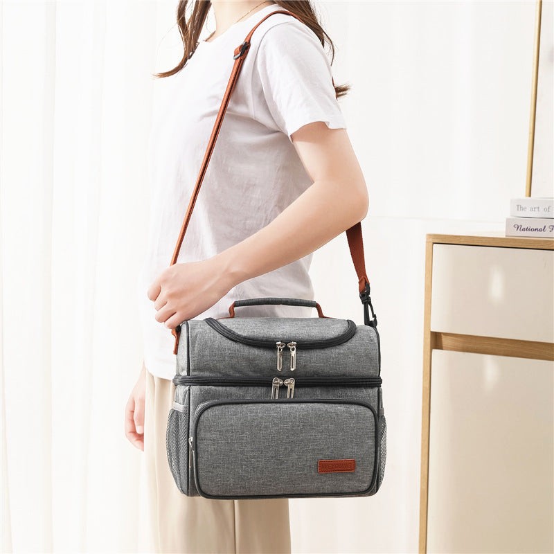 Woman carrying grey insulated lunch bag with ice pack using shoulder strap. Portable cooler tote perfect for daily use and travel.