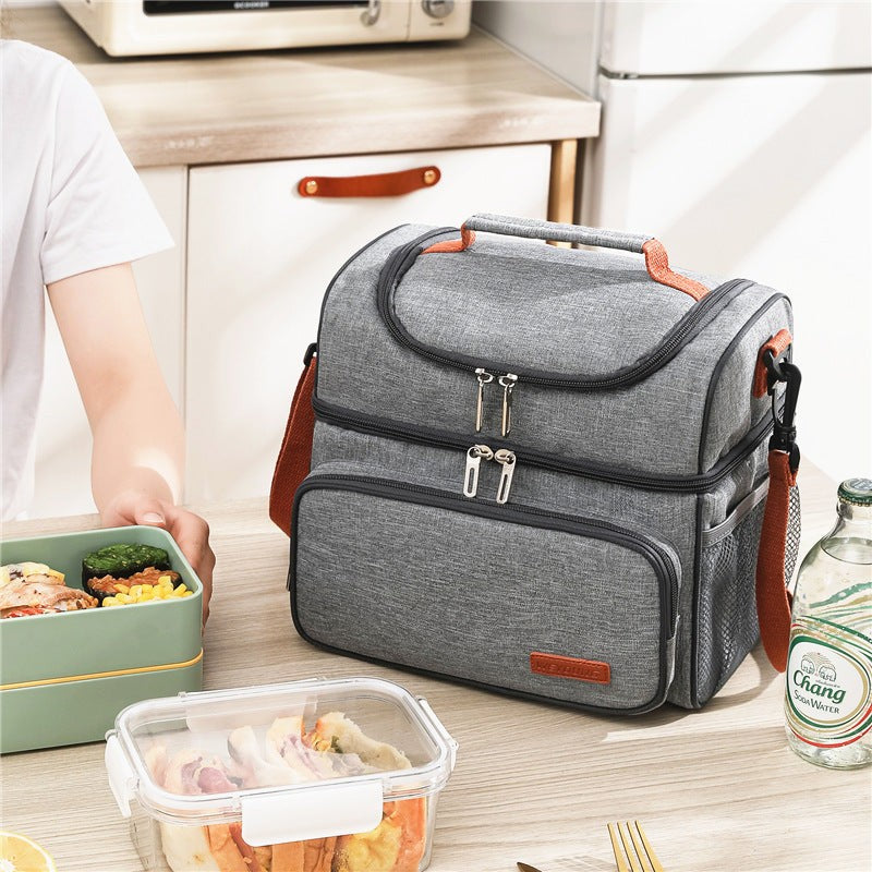 Insulated lunch bag with ice pack in grey, shown on a kitchen table beside food containers. Ideal portable cooler tote for snacks and breastmilk.