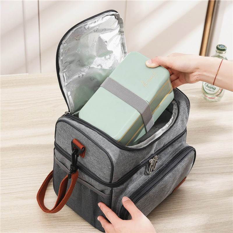 Top view of grey insulated lunch bag with ice pack being packed with a lunch box. Leak-resistant PEVA lining keeps food cold and fresh.