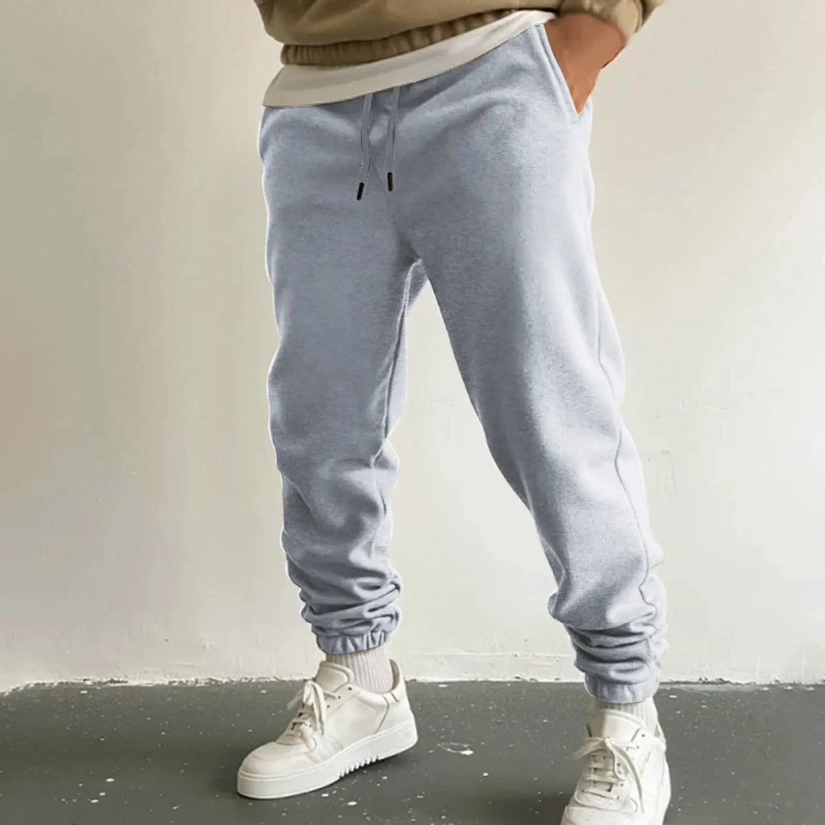 Men’s light gray jogger sweatpants with high waist drawstring and pockets, ankle-length loose fit trousers for running or lounging, styled casually.