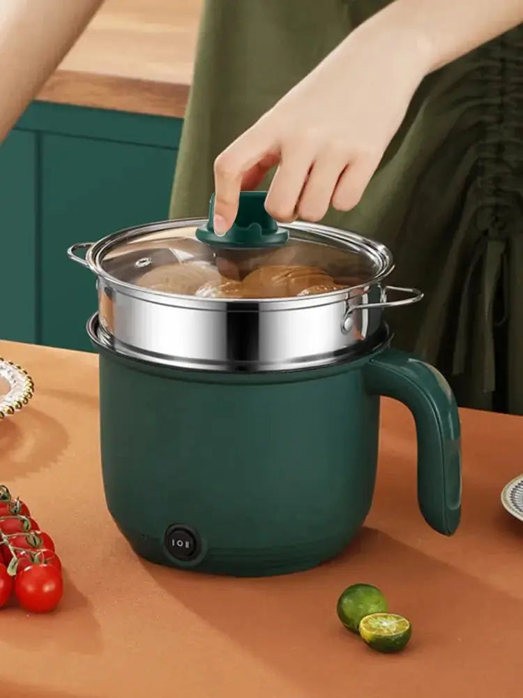 Electric multifunctional cooking pot with transparent lid and steaming tray, shown in use for steaming buns in a modern kitchen setting.