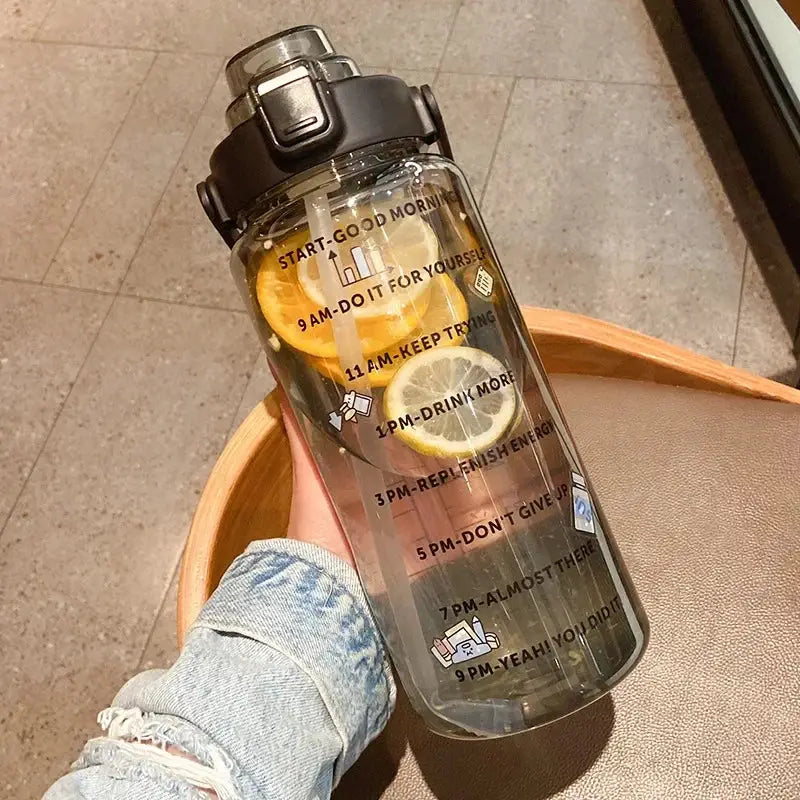 Black 2L sports bottle with straw and time marker, filled with lemon slices and decorated with minimalist stickers for hydration motivation.