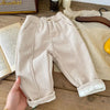 Beige warm winter pants for kids on a wooden table with decor.