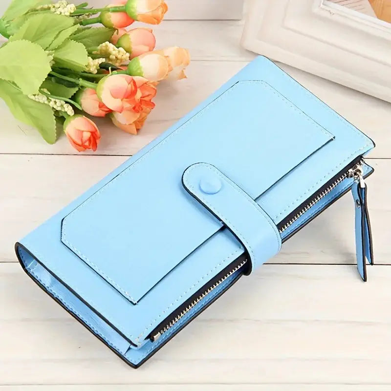 Light blue women's PU leather bifold long wallet with buckle closure and zippered pocket, displayed on a wooden surface with flowers.