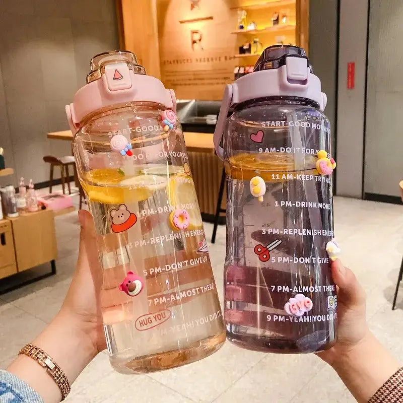 Two 2L fitness water bottles with time markers and straws, one pink and one purple, with citrus slices and playful sticker designs for hydration goals.