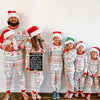 Family in Christmas pajamas with Santa hats holding a sign