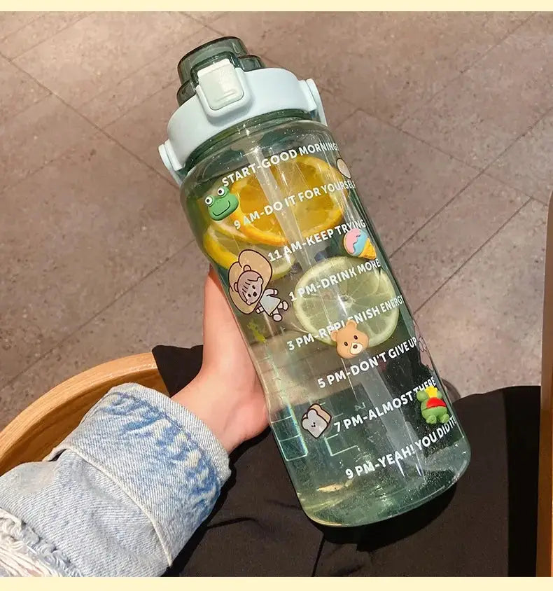 Green 2L water bottle with straw and hourly time marker, decorated with cartoon stickers and filled with lemon slices for summer hydration.