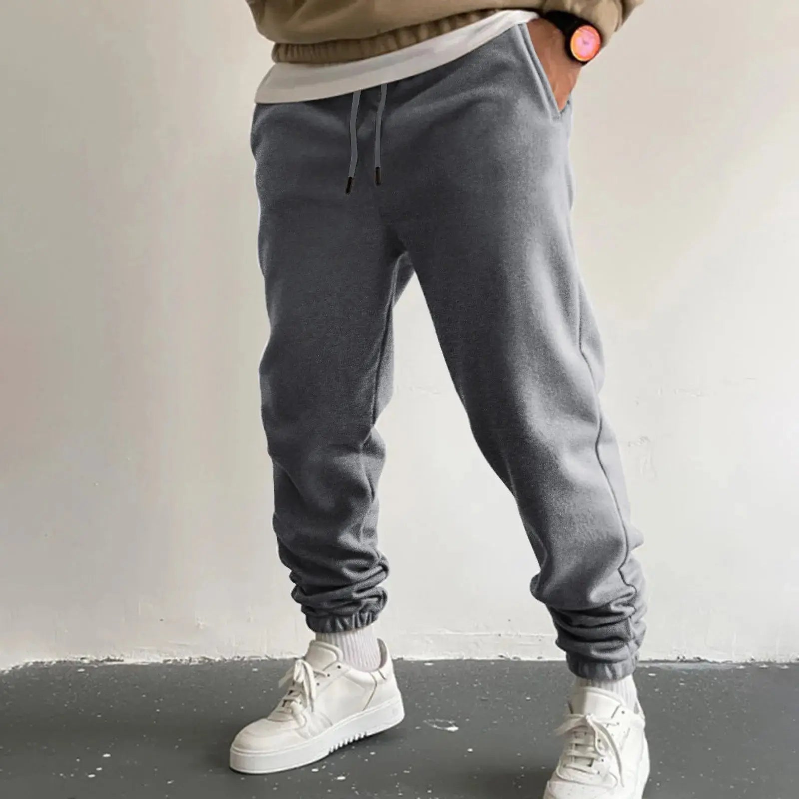 Men’s dark gray jogger sweatpants with high waist drawstring and pockets, loose fit ankle-length trousers for casual or athletic use, styled with sneakers.