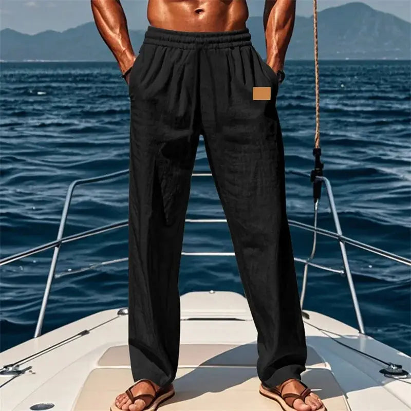 Black men’s loose fit drawstring pants with elastic waistband, ideal for casual or beach outings, shown on a boat with ocean backdrop.