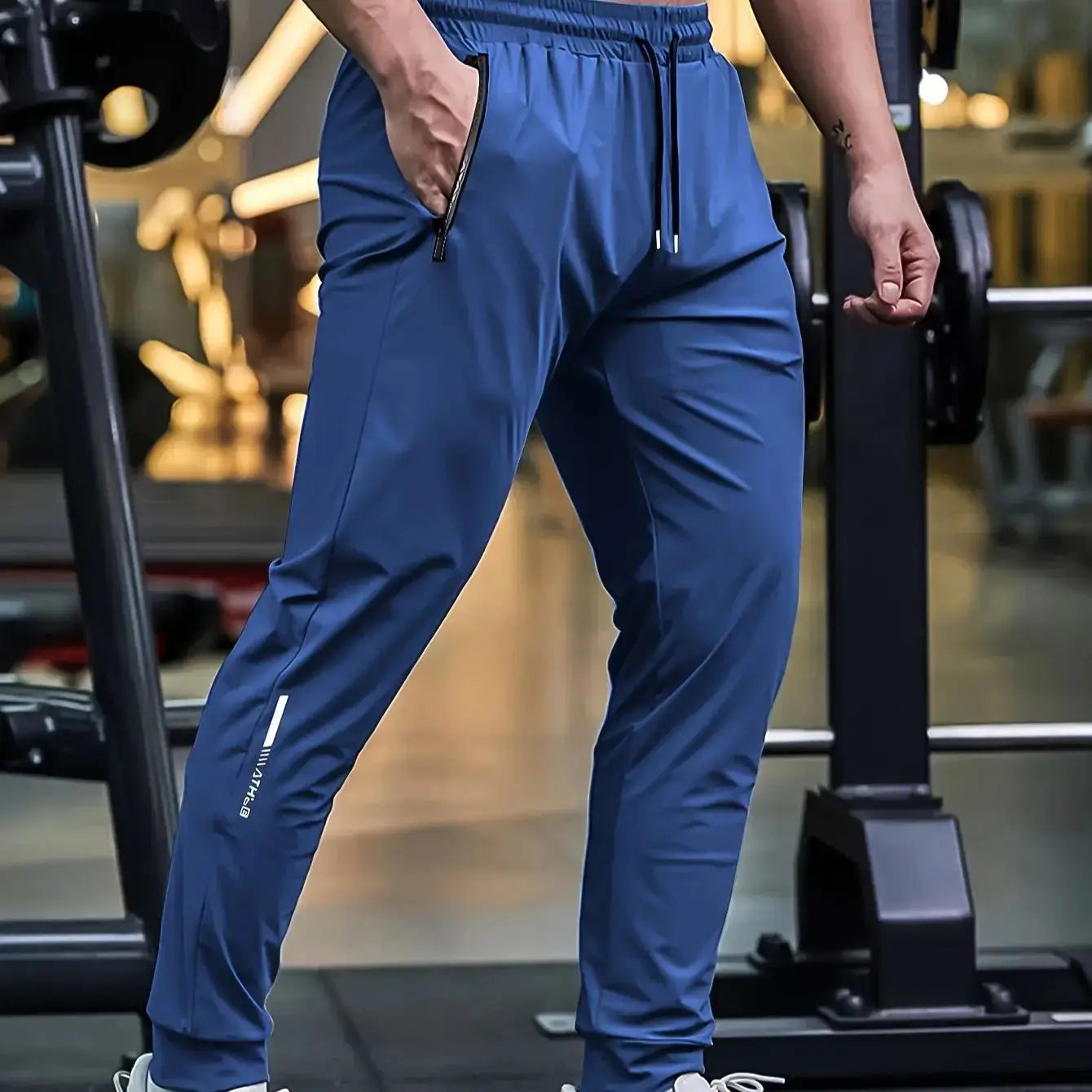 Blue Mens Quick-Dry Training Pants worn in gym setting, featuring tapered fit, drawstring waist, and zippered pockets for active use.