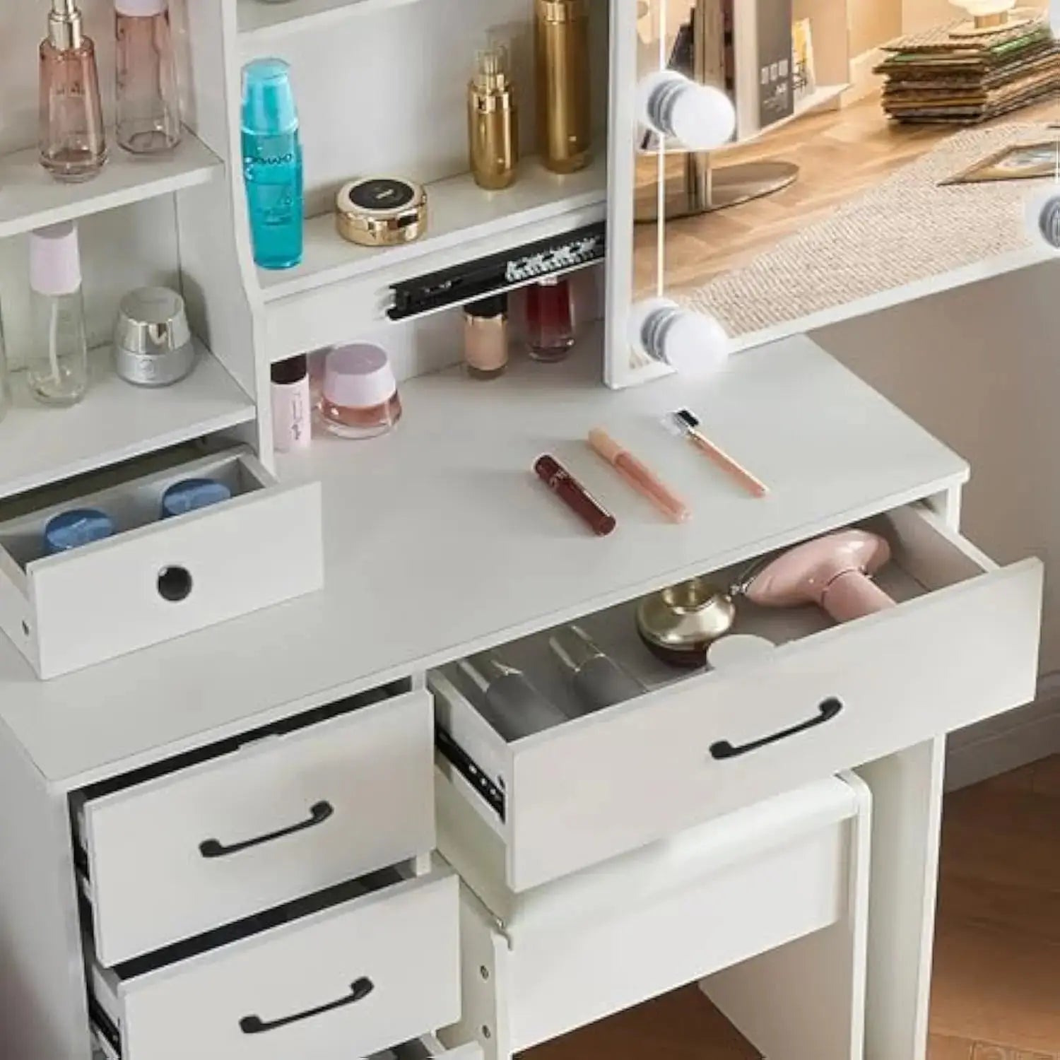 Close-up of makeup vanity table drawers open, showing organized cosmetics and accessories on the white desk with lighted mirror.