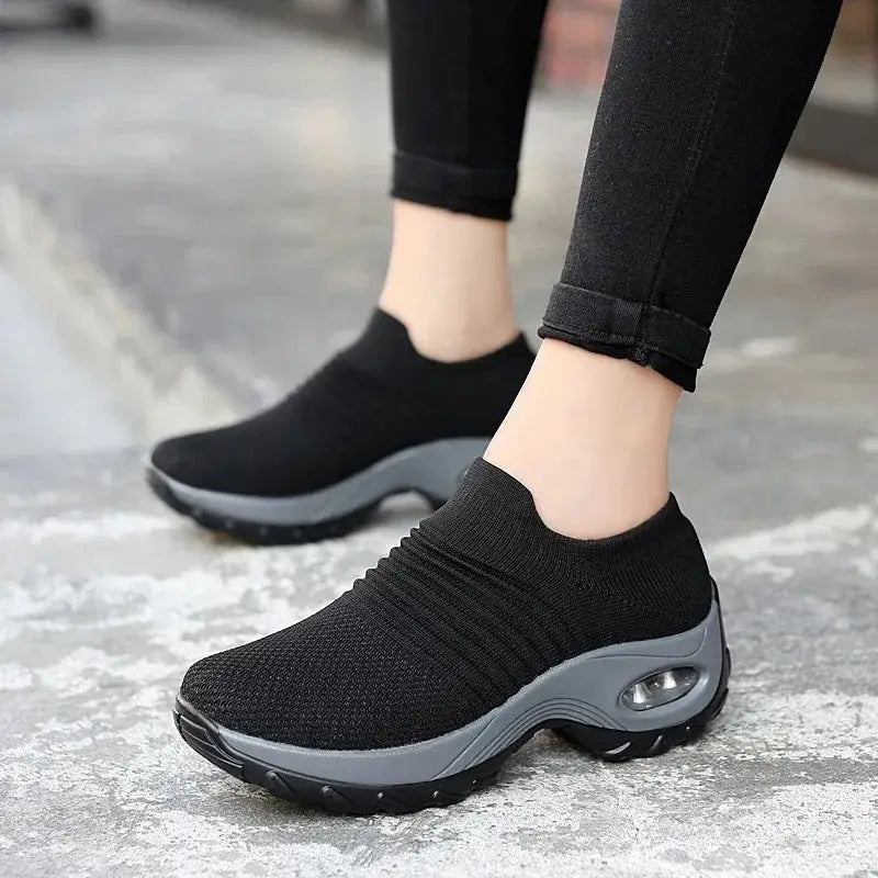 Black women's slip-on sneakers with gray air cushion sole, mesh upper for lightweight comfort during walking, training or casual wear.