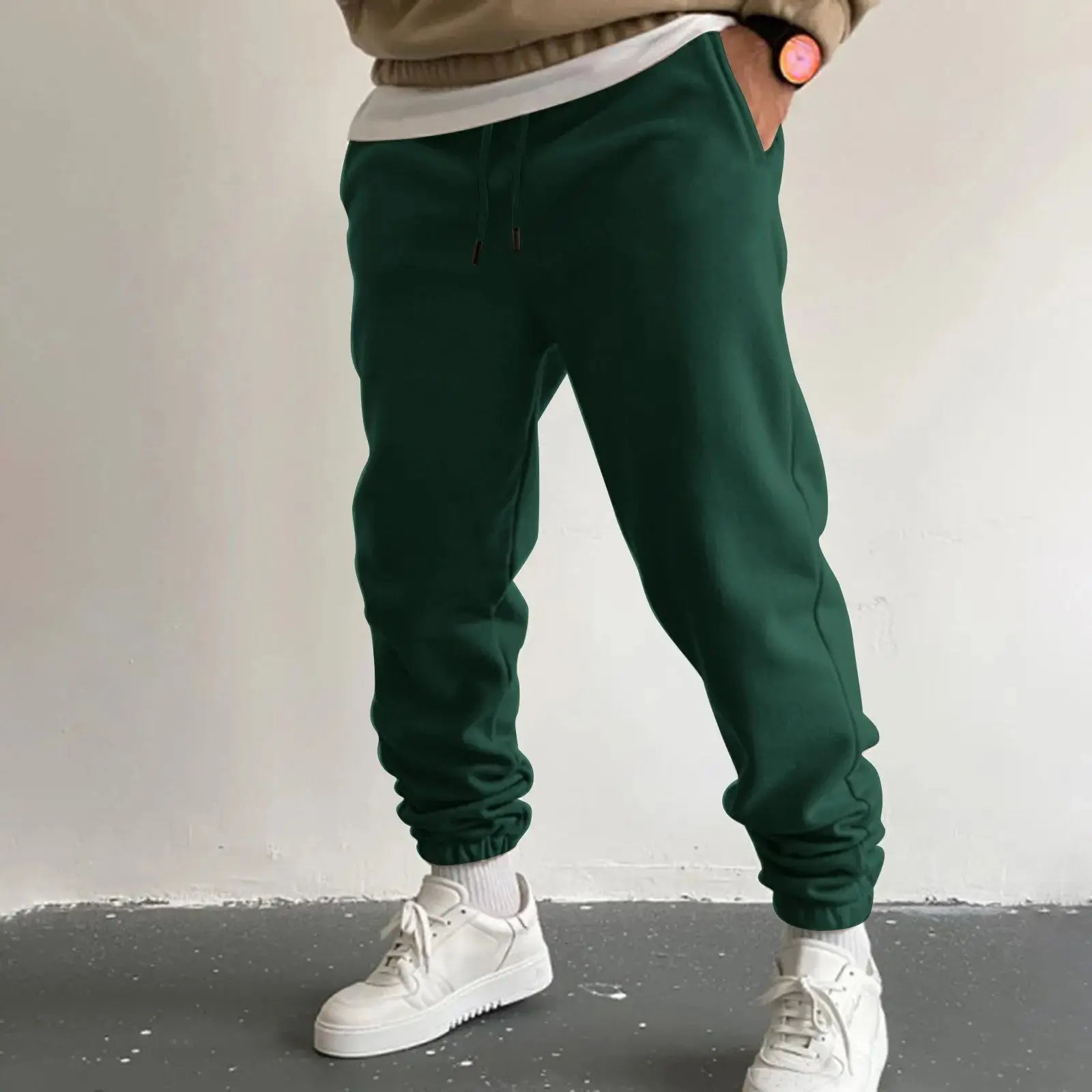 Men’s dark green jogger sweatpants with high waist drawstring and pockets, loose fit trousers for running or everyday wear, paired with white sneakers.