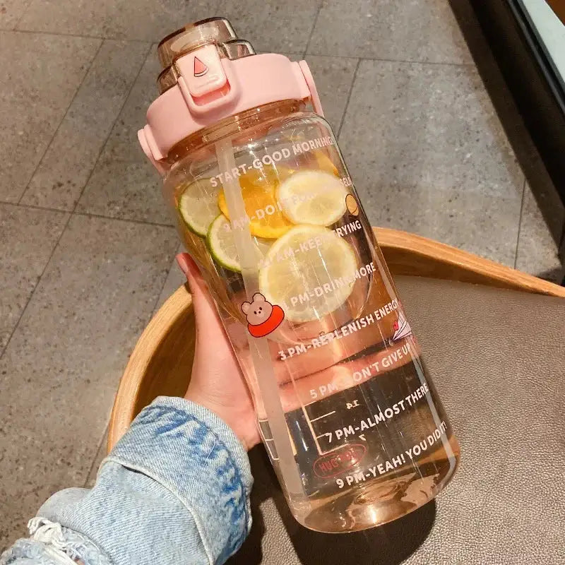 Pink 2L water bottle with straw and time marker, featuring citrus slices and motivational stickers for daily hydration and energy boost.