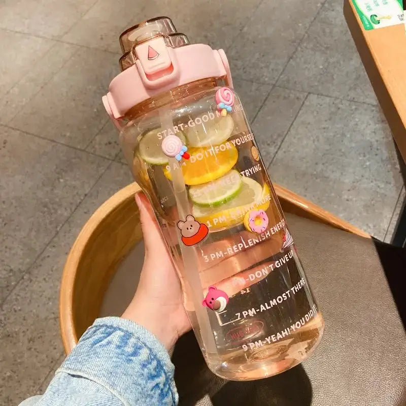 Pink 2L sports water bottle with straw and time marker, filled with citrus fruits and adorned with cute character stickers for hydration tracking.