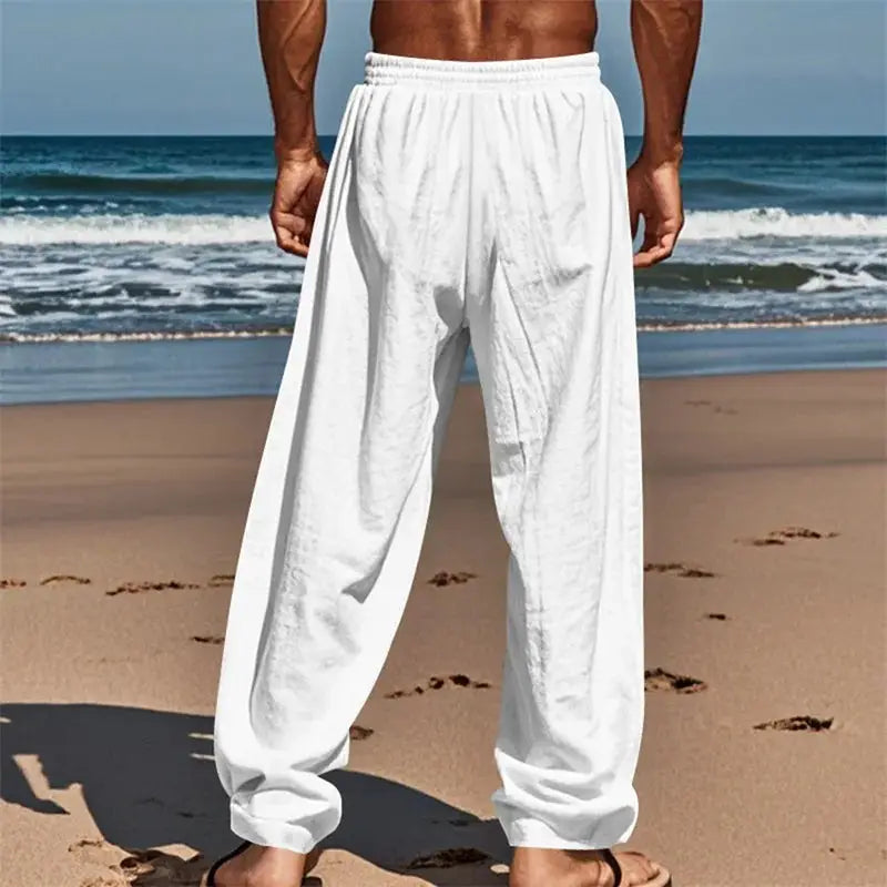 White men’s breathable drawstring pants with elastic waistband and loose fit, perfect for beachwear, shown from the back on sandy shore.