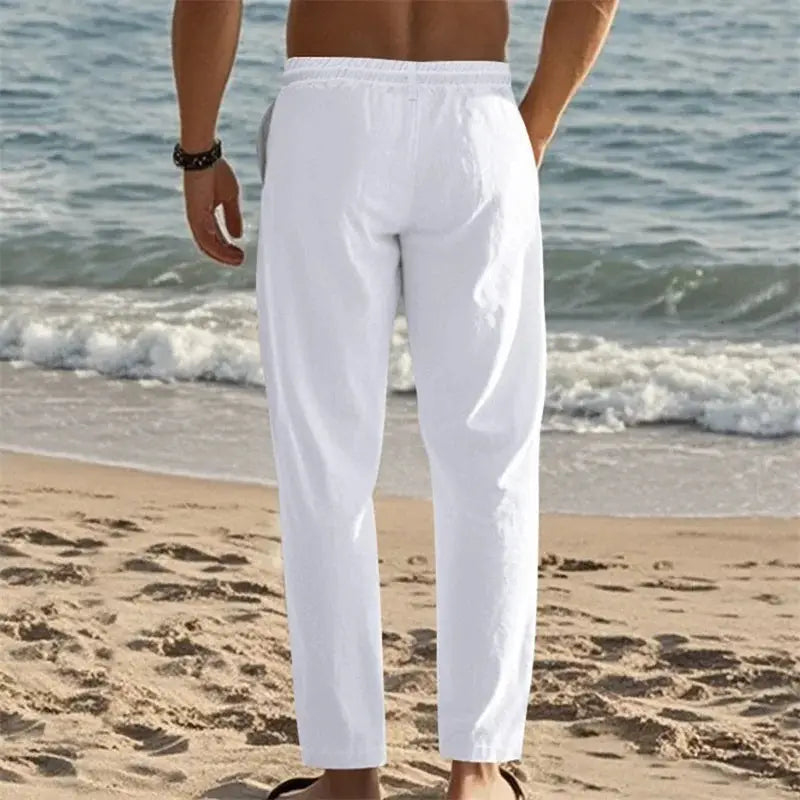 Men's lightweight linen pants with drawstring and pockets in white, ideal for beach and casual summer wear, shown on a man standing by the ocean.