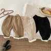 Warm winter pants for kids in three colors laid out on a bed.