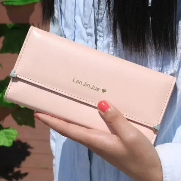 Blush pink Women's Long PU Leather Trifold Wallet held in hand, featuring gold Lan Jin Jue logo and heart detail for elegant style.