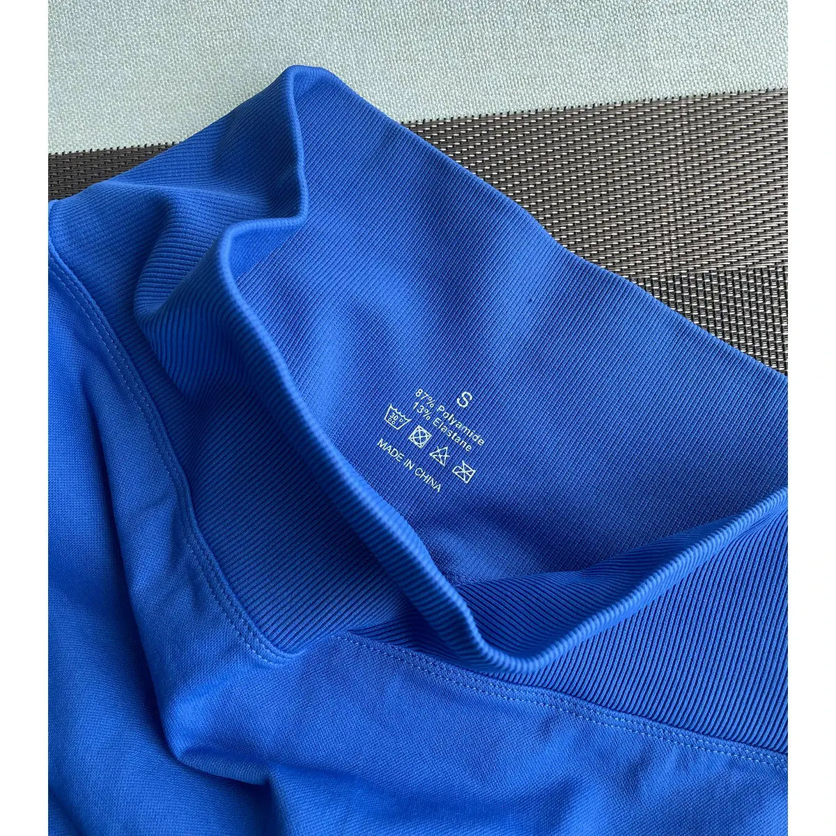 Close-up of blue Women's 2-Piece Seamless Workout Set showing size S label and care instructions on waistband. Made of nylon and spandex for activewear.