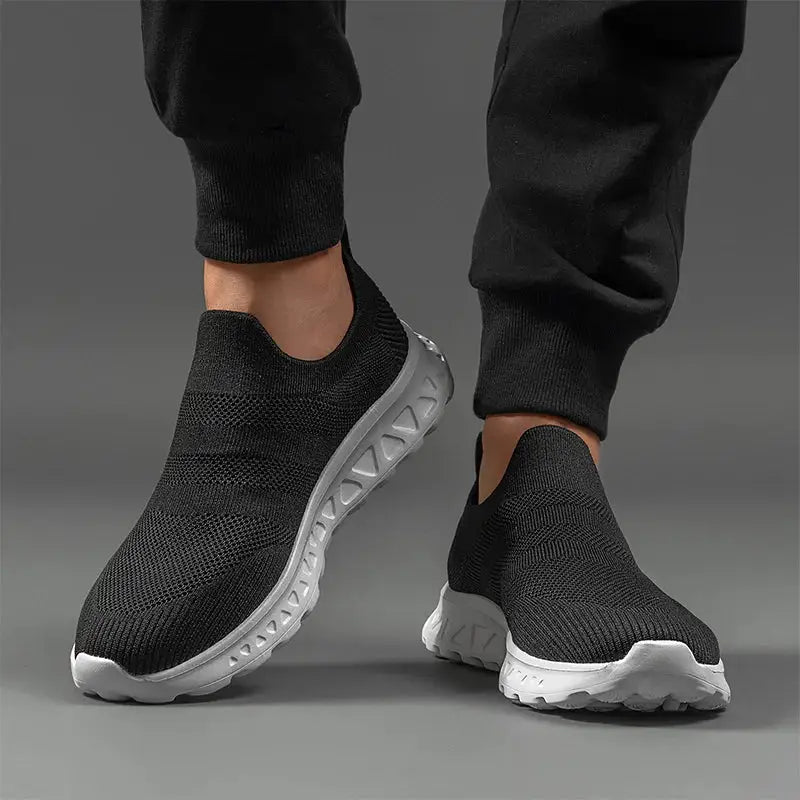 Front view of black breathable mesh men’s slip-on sneakers with cushioned sole, ideal for sports, walking, or casual wear.