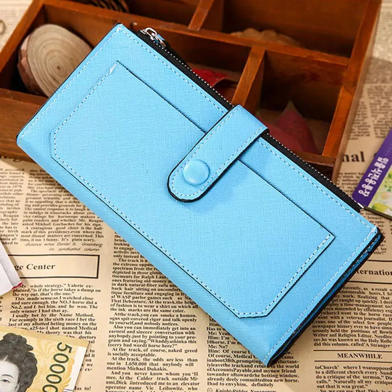 Sky blue women's PU leather bifold long wallet with buckle strap and zippered pocket, placed on a rustic newspaper surface.