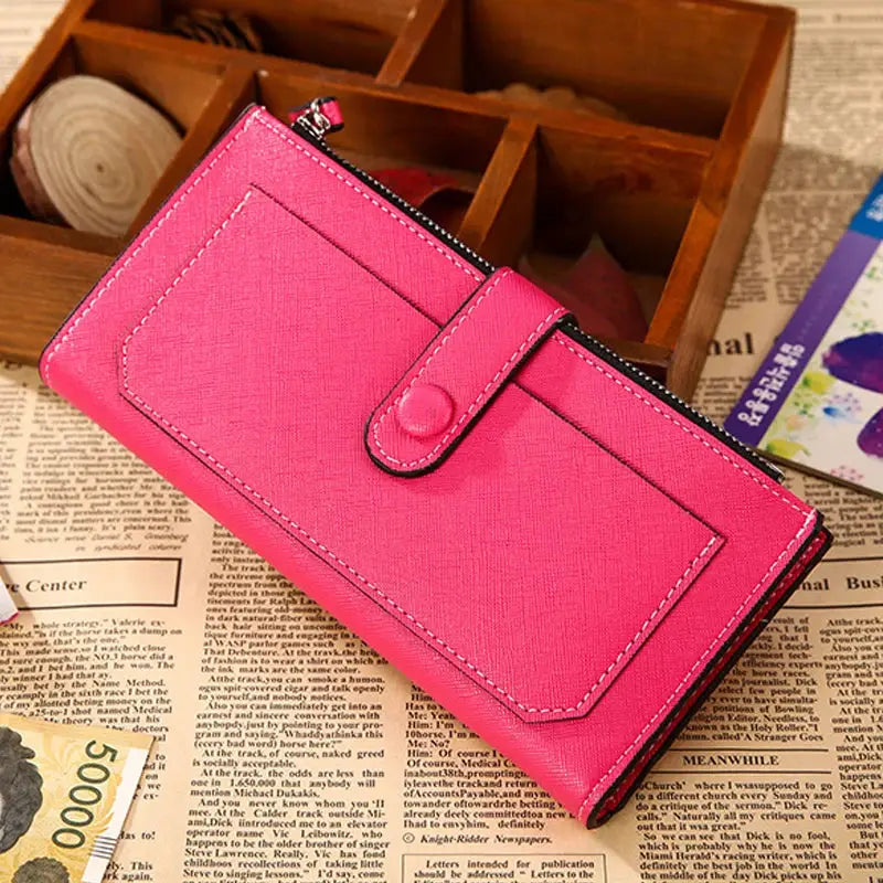 Hot pink women's PU leather bifold long wallet with buckle strap and zippered compartment, styled on a newspaper background.
