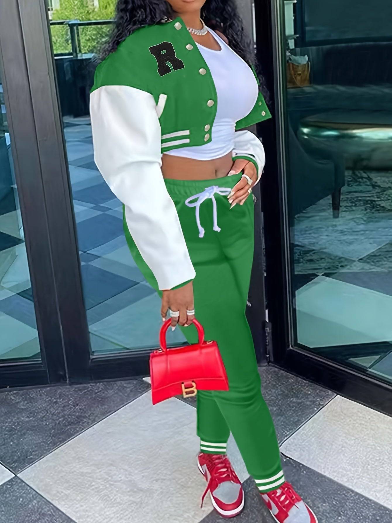 Green crop top varsity jacket and jogger pants set for women, styled with red sneakers and a red handbag for a trendy streetwear look.